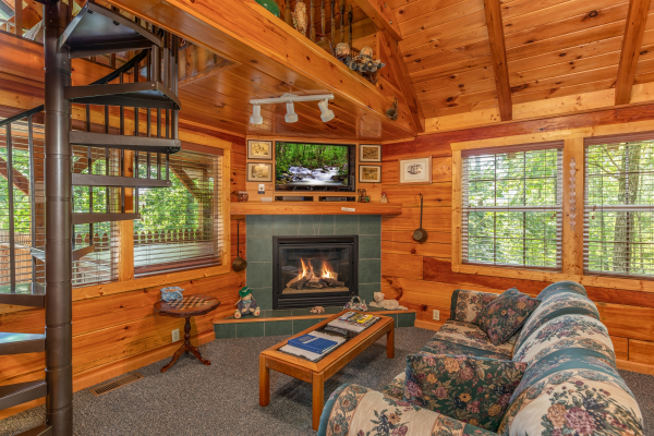 Fireplace, TV, sofa, and spiral staircase in the living room at Just Us, a 1 bedroom cabin rental located in Pigeon Forge