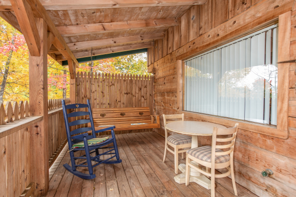 Outdoor seating with a porch swing rocking chair and dining space for two at All Shook Up, a 1 bedroom cabin rental located in Pigeon Forge