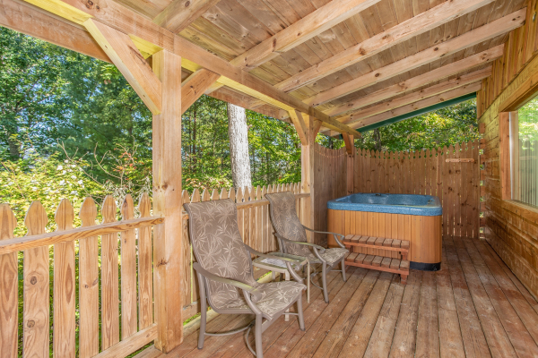 Hot tub and two chairs on a covered deck at Forever Yours, a 1-bedroom cabin rental located in Pigeon Forge