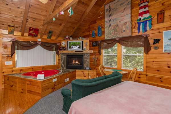 A studio concept living space with bed, loveseat, jacuzzi, fireplace, and TV at Forever Yours, a 1-bedroom cabin rental located in Pigeon Forge