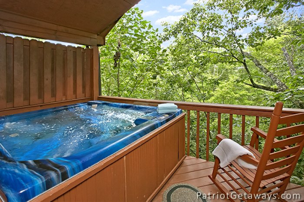 rocking chair and hot tub on a covered porch with a woods view at always together forever a 1 bedroom cabin rental located in pigeon forge