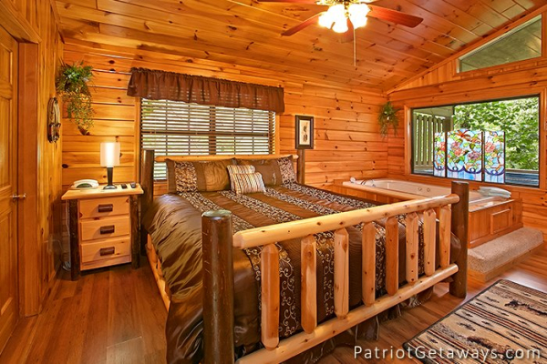 king sized log bed next to a jacuzzi at always together forever a 1 bedroom cabin rental located in pigeon forge