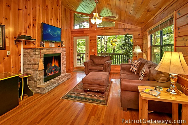living room with a sofa large chair stone fireplace and television at always together forever a 1 bedroom cabin rental located in pigeon forge