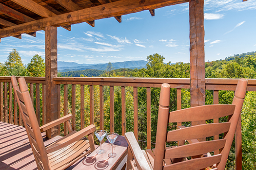 Two rocking chairs with drinks on the table overlooking mountains at A Postcard View, a 1 bedroom cabin rental located in Pigeon Forge