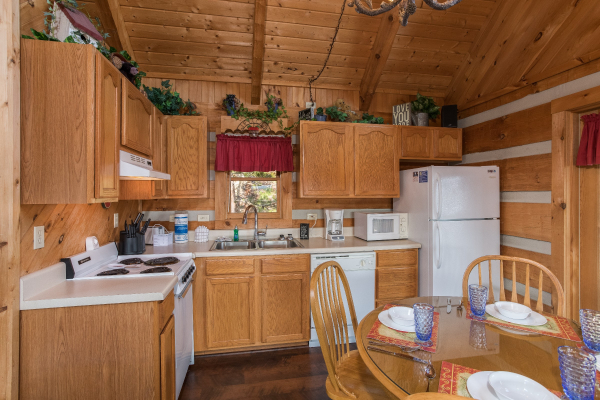 Kitchen with white appliances and dining room table for four at A Postcard View, a 1 bedroom cabin rental located in Pigeon Forge