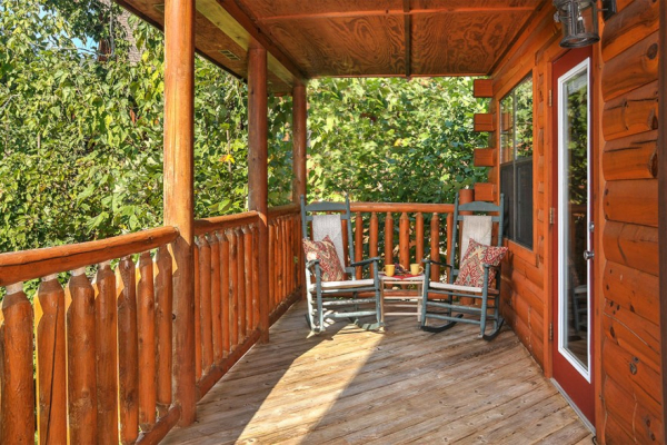 Covered deck with rocking chairs and wooded surround at Kick Back & Relax! A 4 bedroom cabin rental located in Pigeon Forge