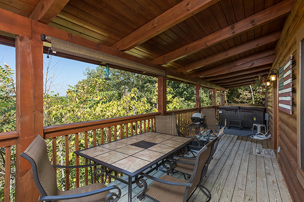 Covered deck dining space for four with a grill and hot tub in the background at Lake Life, a 4 bedroom cabin rental located in Sevierville