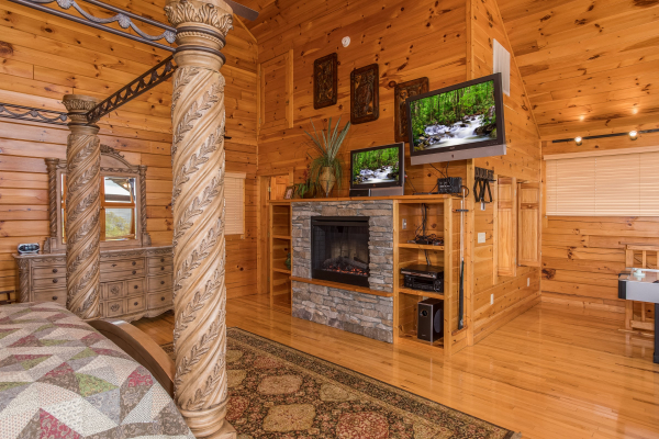 Loft room with a king canopy bed, fireplace, and two TVs at Howlin' in the Smokies, a 2 bedroom cabin rental located in Pigeon Forge