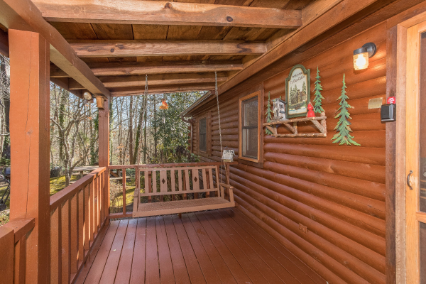 Swing on a covered deck at Snuggle Inn, a 2 bedroom cabin rental located in Pigeon Forge