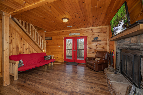 Futon, fireplace, TV, and deck access at Wonders in the Sky, a 3 bedroom cabin rental located in Gatlinburg
