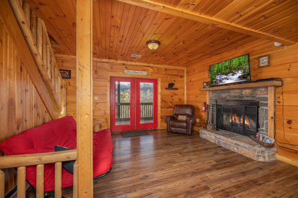 Lower living room with futon, fireplace, TV, and deck access at Wonders in the Sky, a 3 bedroom cabin rental located in Gatlinburg