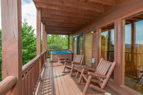 Log rocking chairs and a hot tub on a covered deck at Mountain Bliss, a 2 bedroom cabin rental located in Pigeon Forge