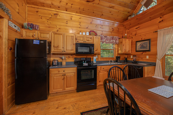 Dining space for six and kitchen with black appliances at Firefly Ridge, a 2 bedroom cabin rental located in Pigeon Forge