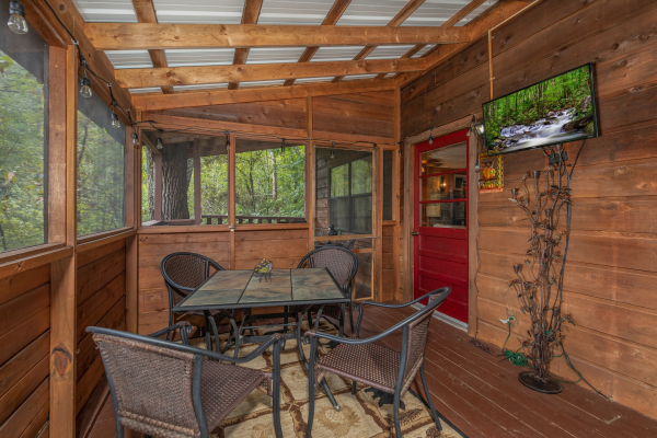 Screened in porch with dining space for four and a TV at Misty Mountain Sunrise, a 3 bedroom cabin rental located in Pigeon Forge