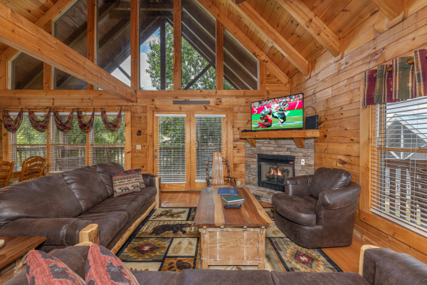Living room with fireplace, TV, seating, and large windows at Logged Inn, a 3 bedroom cabin rental located in Pigeon Forge