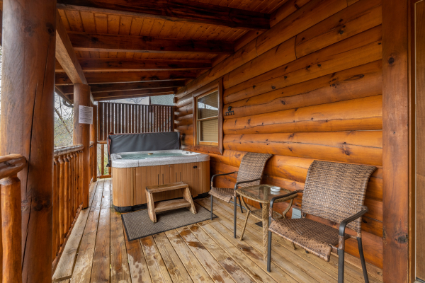 Hot tub and chairs on a covered deck at Absolutely Wonderful, a 2 bedroom cabin rental located in Pigeon Forge