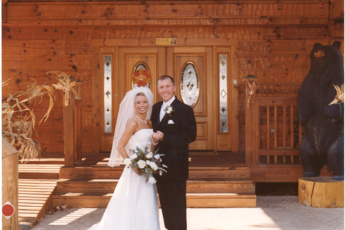 Newlyweds standing in front of Big Bear Lodge, a 7-bedroom cabin rental located in Gatlinburg