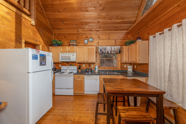 Dining table and kitchen with white appliances at Just You and Me Baby, a 1 bedroom cabin rental located in Gatlinburg
