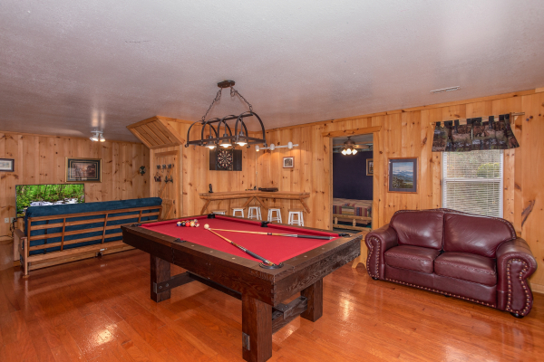 Red felted pool table and a loveseat in the game room at Bearly in the Mountains, a 5-bedroom cabin rental located in Pigeon Forge
