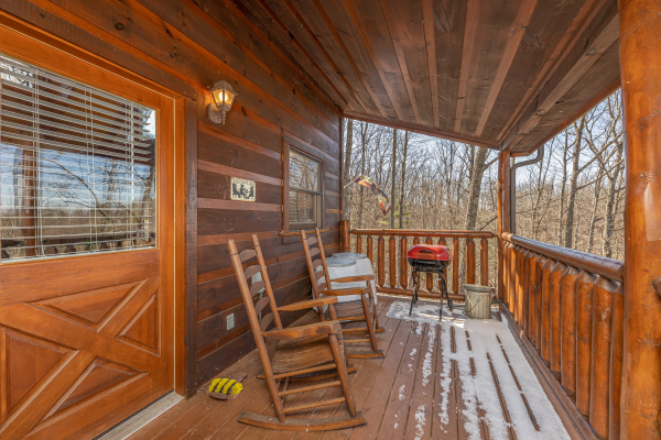 Deck rocking chairs and a grill on a covered deck at Honey Bear Haven, a 1 bedroom cabin rental located in Pigeon Forge