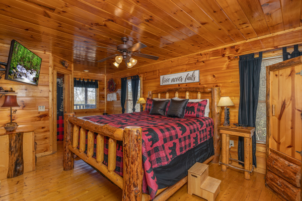 Bedroom with a king log bed, night stands, lamps, and a TV at Honey Bear Haven, a 1 bedroom cabin rental located in Pigeon Forge