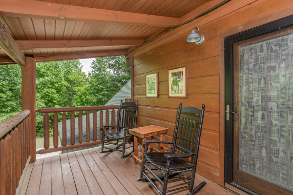 Black rocking chairs and a small table on a covered deck at Aw Paw's Place, a 1-bedroom cabin rental located in Pigeon Forge